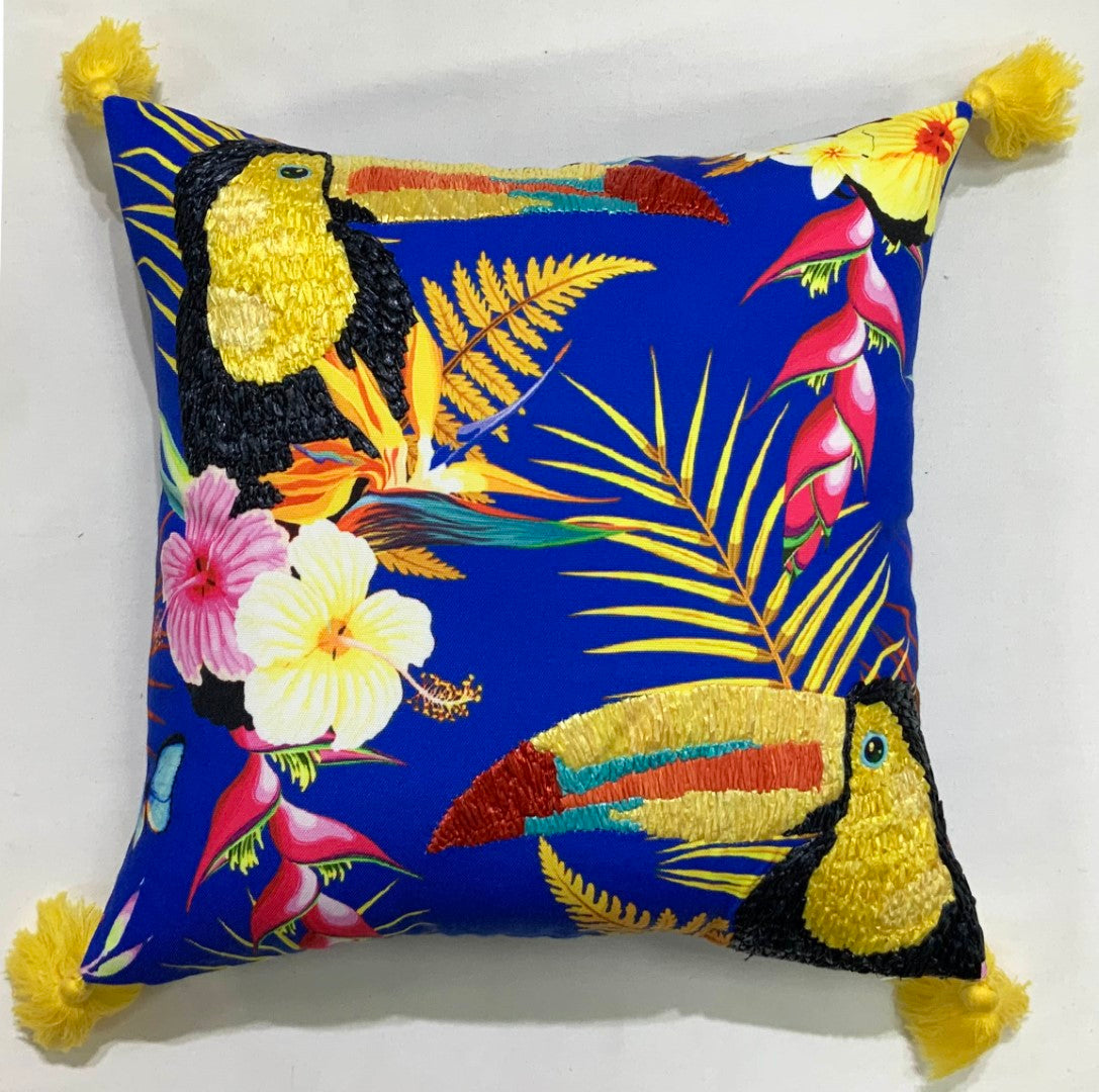 Two embroidered toucans among hibiscus and palms on a pillow with yellow tassels