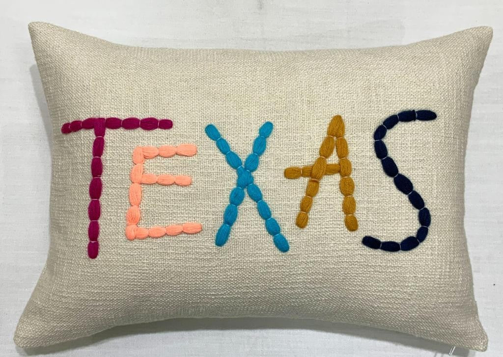 Lumbar pillow with TEXAS spelled in sunset-colored loop embroidery on a natural base